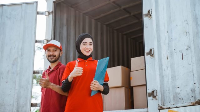 female worker wearing a hijab and a delivery man wearing a red uniform with thumbs up behind a logistics container